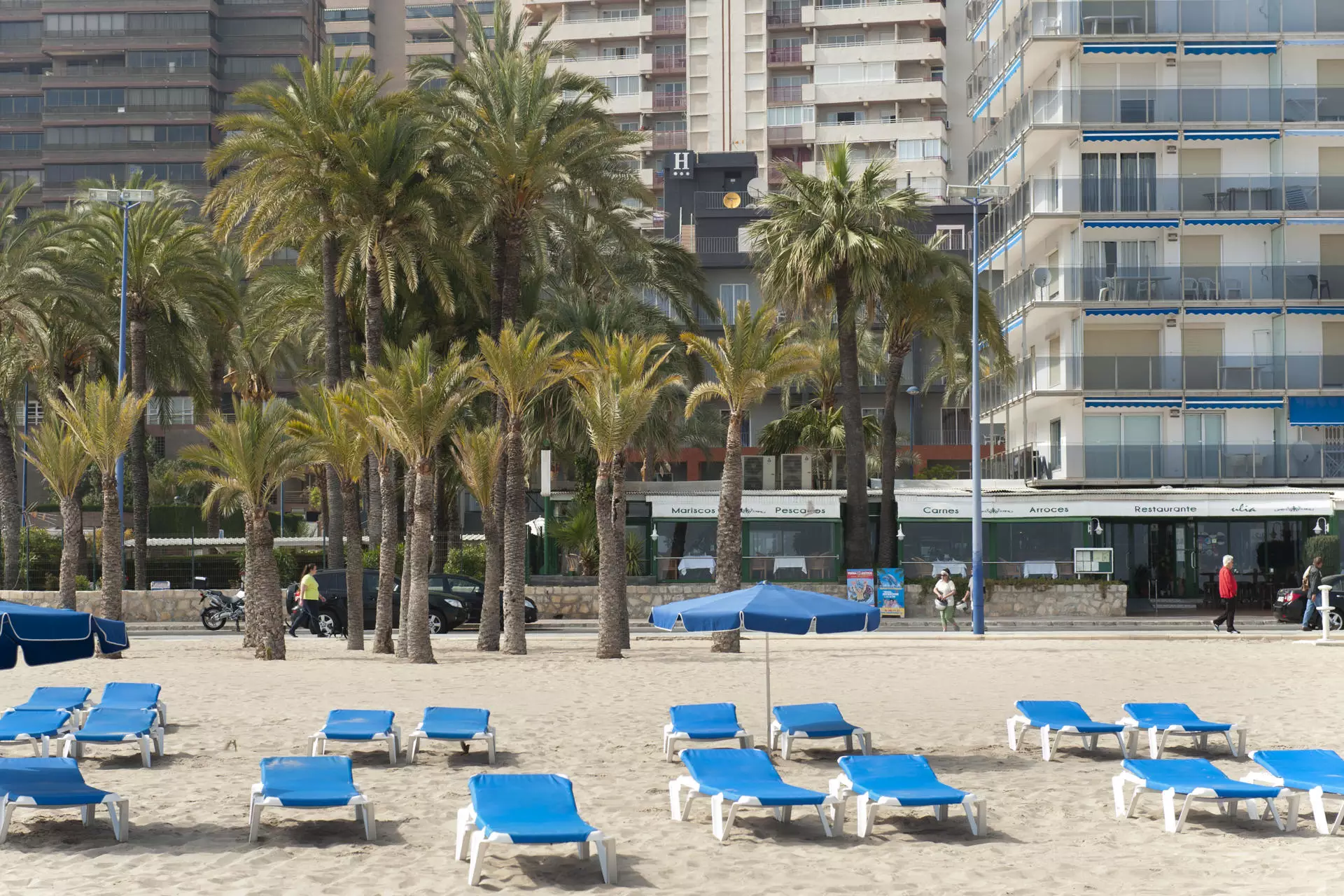Foto de la playa de Benidorm con el Hotel Palmeral de fondo y unas tumbonas azules